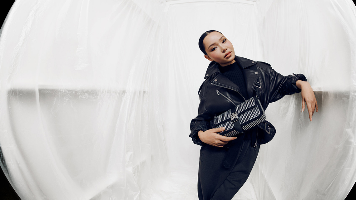 Ein Outfit aus der HUGO Herbst/Winter 2023 Kollektion: eine Frau trägt eine Lederjacke und eine auffällige Lederhandtasche.