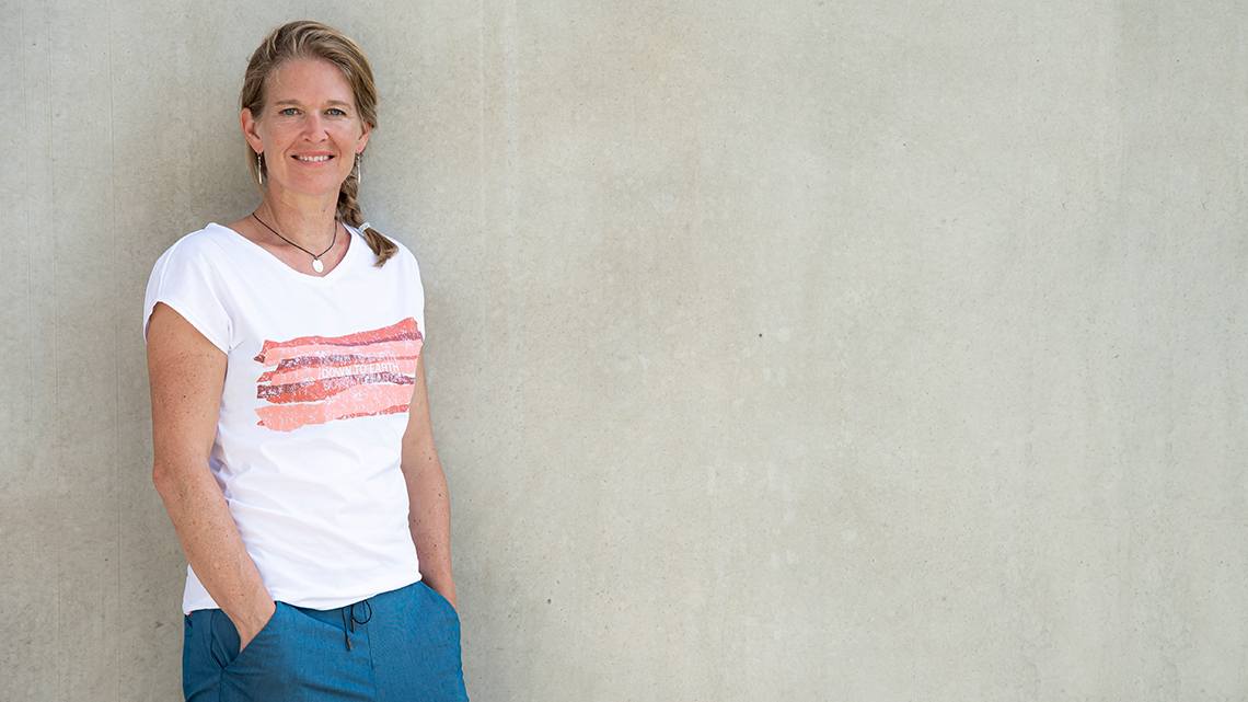 Antje von Dewitz, Geschäftsführerin von VAUDE, lehnt an einer grauen Wand und trägt ein weißes T-Shirt mit rotem Druck.
