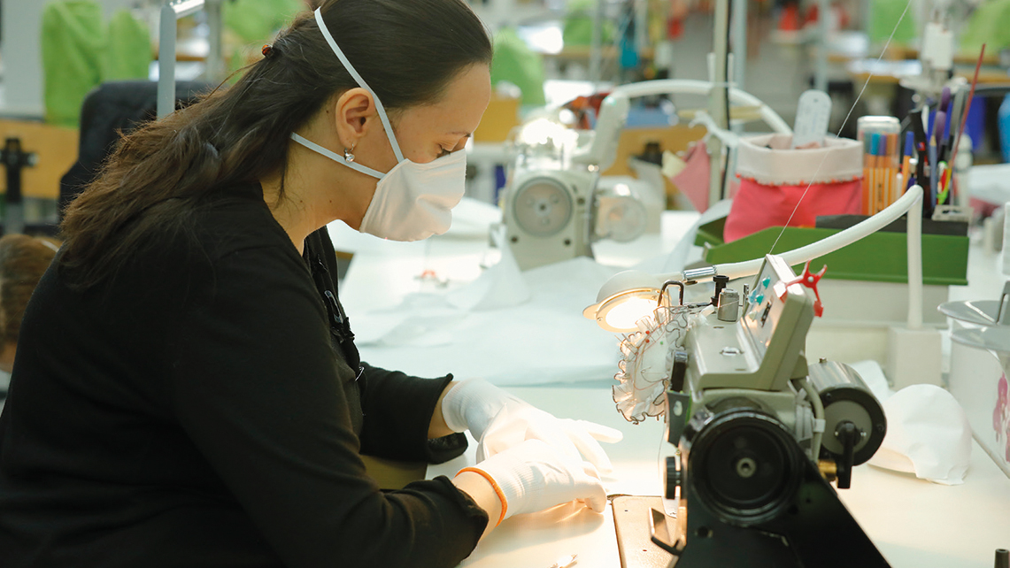 Frau mit Maske an Nähmaschine produziert Masken