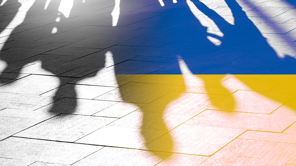 Die Schatten verschiedener Menschen sind auf dem Pflaster zu erkennen, einige Schatten leuchten in den Farben der Ukraine.