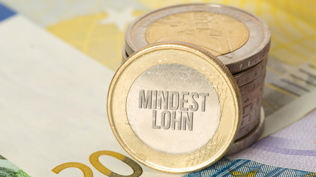 Auf mehreren Geldscheinen liegt ein Stapel Münzen, auf einer steht "Mindestlohn".