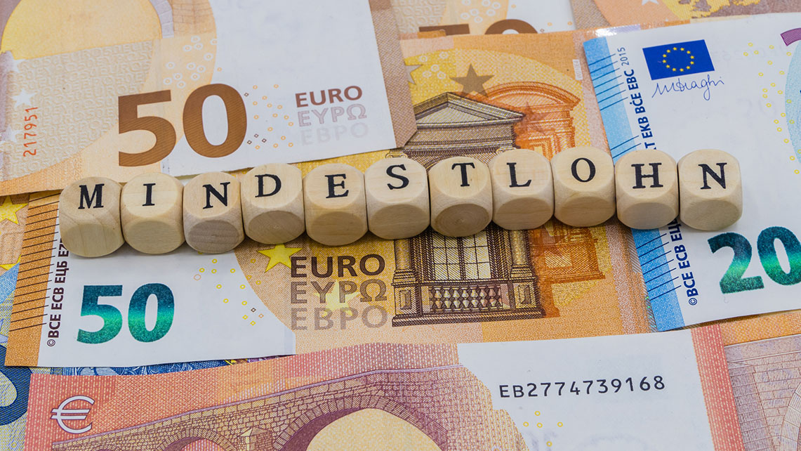 Holzwürfel mit Buchstaben bilden das Wort Mindestlohn und liegen auf mehreren Euroscheinen