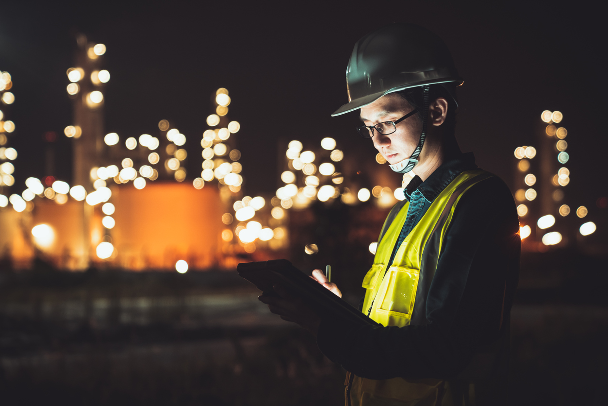 Asiatischer Mann Ingenieur mit digitalem Tablet arbeitet in der Spätnachtschicht in einem Industriegebiet.