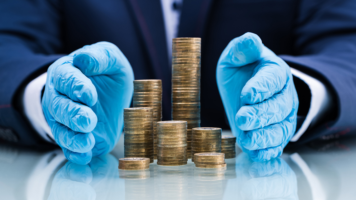Zwei Hände in blauen Schutzhandschuhen schirmen Stapel mit Münzen nach rechts und links ab.