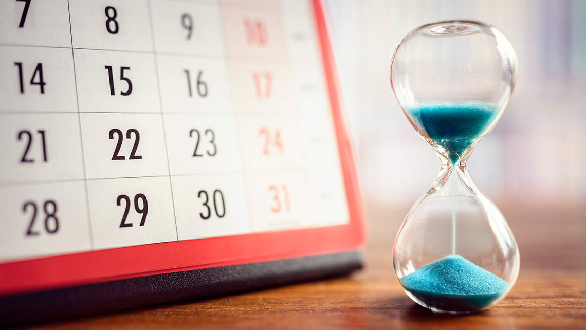 Sanduhr mit blauem Sand steht vor einem Kalender