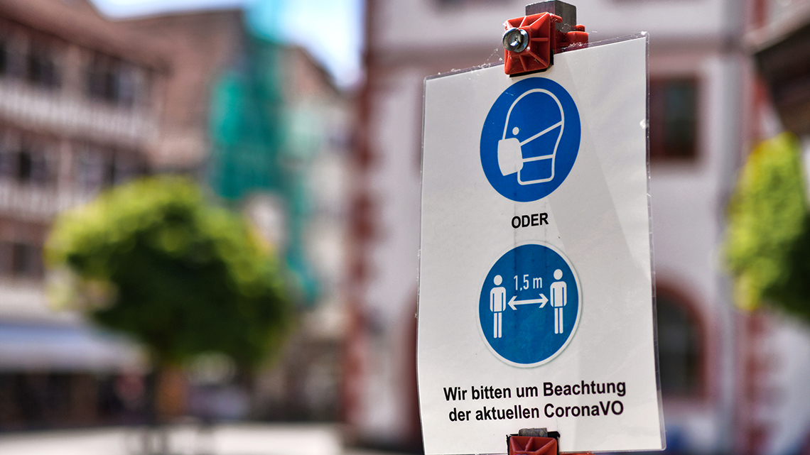 In der Innenstadt ist auf einem Schild ein Symbol zum Tragen einer Maske und zum Einhalten des Abstands von 1,50 Meter mit Verweis auf die Coronaverordnung zu sehen.
