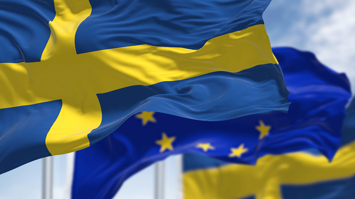 Vor einem bewölkten Himmel wehen die schwedische und die europäische Fahne im Wind.
