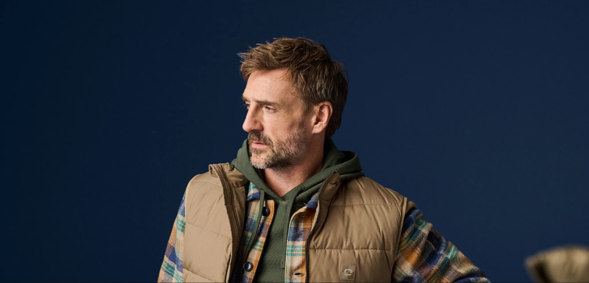 bärtiger Mann mit Karojacke, Hoody und beiger Weste