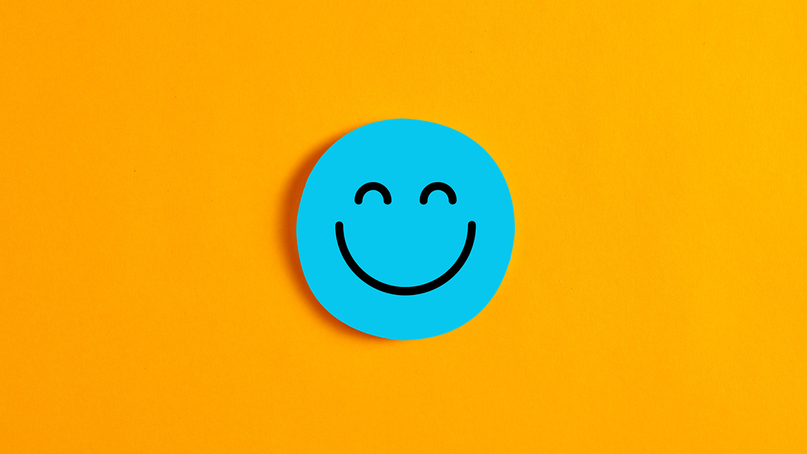 Auf einem orangfarbenem Hintergrund liegt ein ausgeschnittenes blaues Papiersmiley