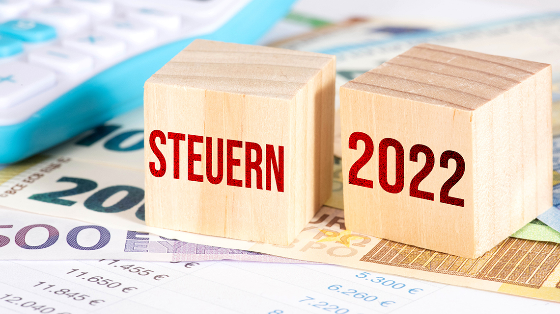 Auf mehreren Geldscheinen liegen zwei Holzwürfel mit der Schrift "Steuern" und "2022".