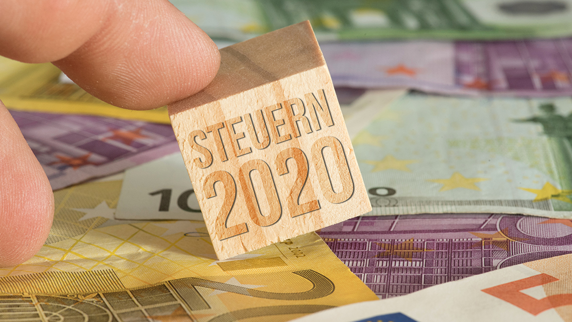 Hand hält Holzwürfel mit Schrift Steuer 2020 auf Eurogeldscheinen