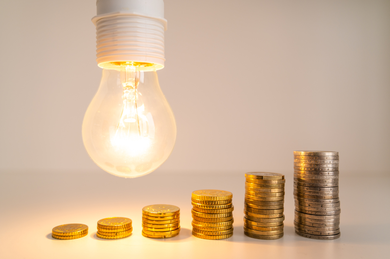Beleuchtete Glühbirne mit Münzen daneben. Energietarife steigen.