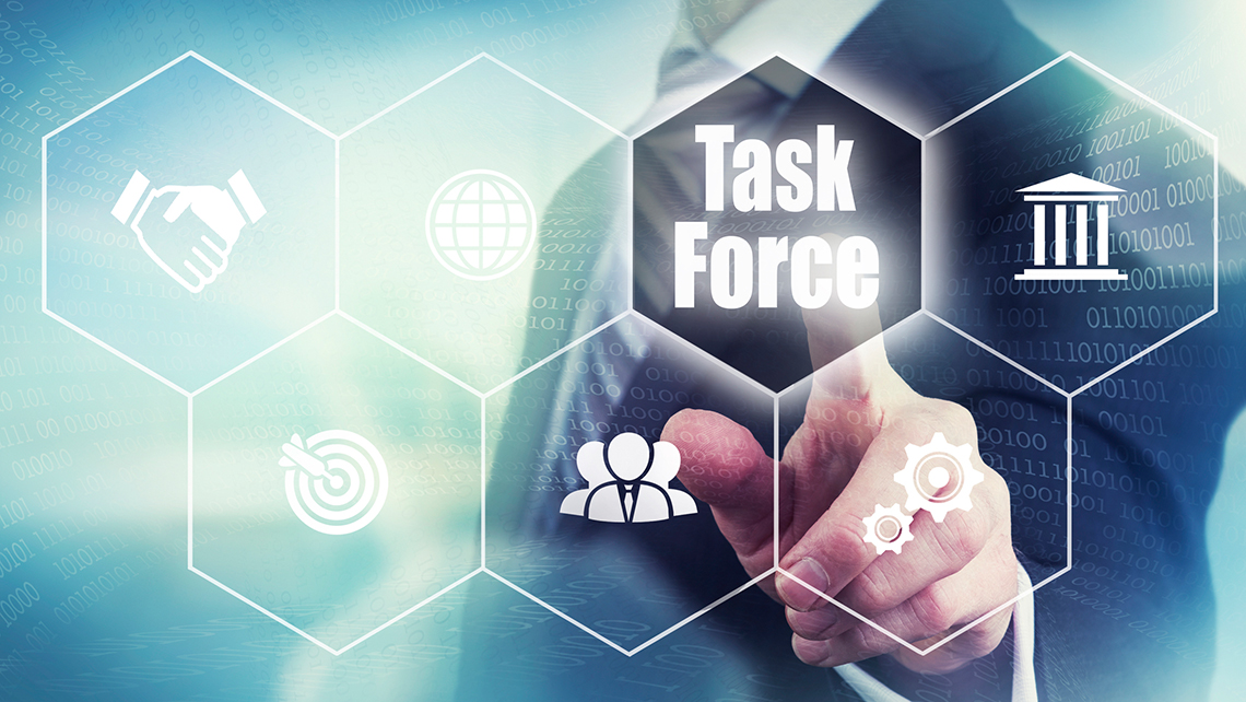 Ein Mann im Anzug zeigt auf das Wort Task Force, das zwischen anderen Symbolen auf einer virtuellen Wand aufleuchtet.