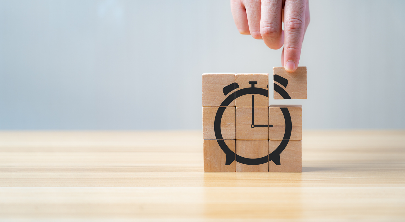 Uhr aus Holzklötzen bei der eine Hand ein Holzstück ergänzt