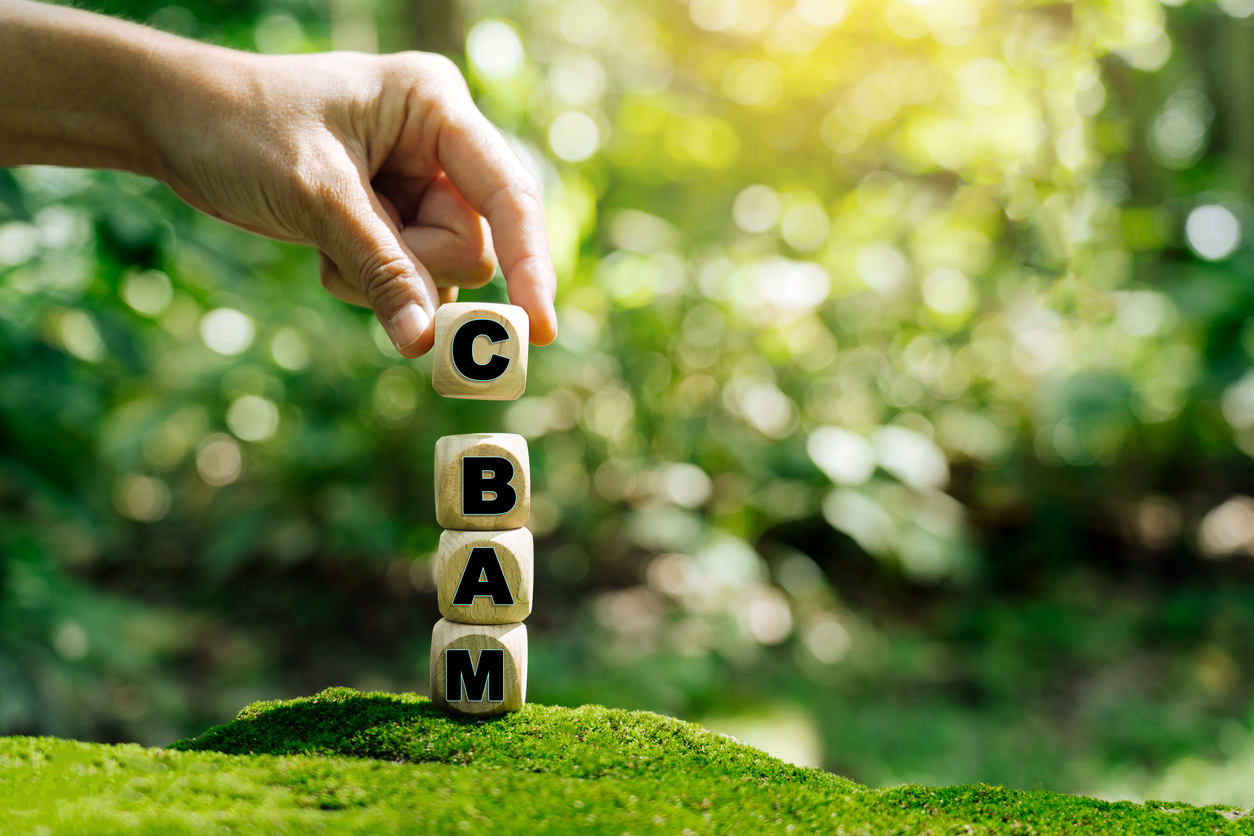 The first carbon-tariff system, the EU Carbon Border Adjustment Mechanism (CBAM) as a grapic with letters on dices and a finger in a green environment