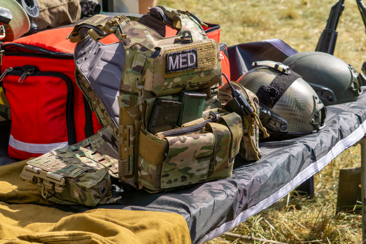 Taktische Weste mit "MED"-Aufnäher, Helme und eine rote medizinische Tasche auf einem Feldtisch – militärische Sanitätsausrüstung