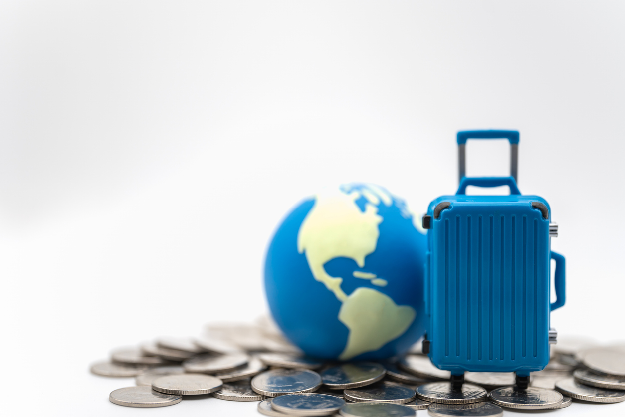 Reisekoffer mit Weltkugel daneben auf Münzen