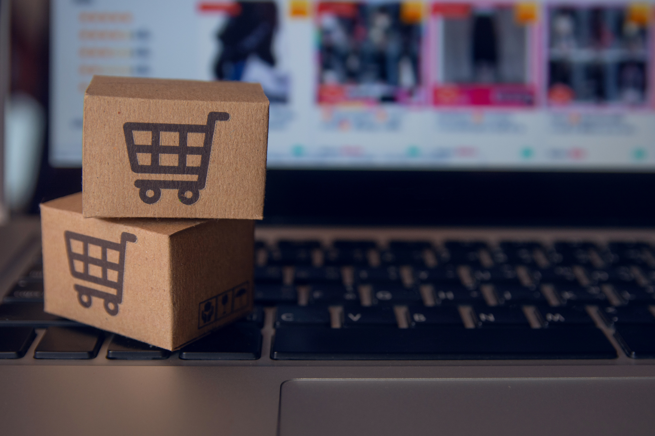Kleine Kartonpakete auf Laptoptastatur, im Hintergrund Online-Shopping Portal